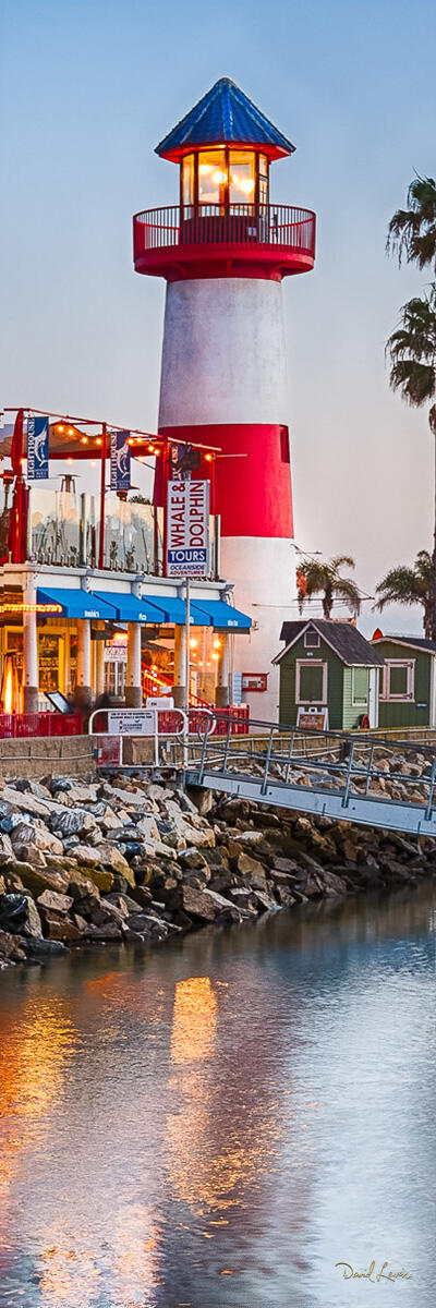 Oceanside Harbor Village Lighthouse at Dusk Vertical photograph of the Oceanside Harbor Village lighthouse at dusk with warm evening light, harbor reflections, and coastal buildings.